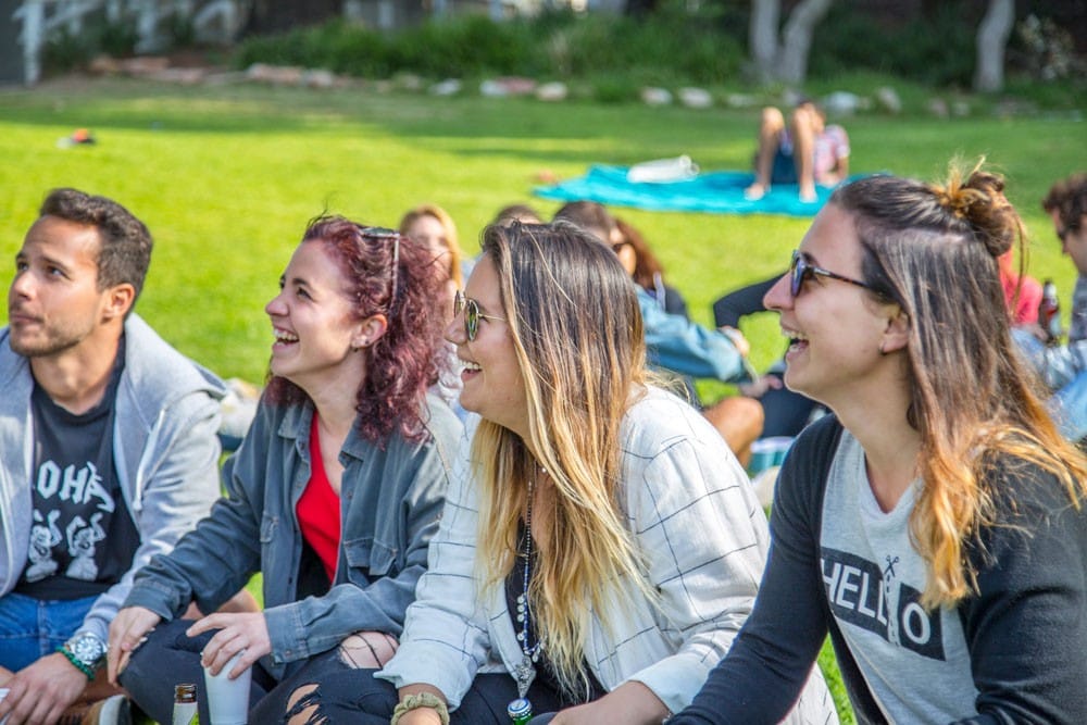 grupos Facebook buscar trabajo grupo de amigos mirando de perfil a cámara y sonriendo. Están sentados en el césped